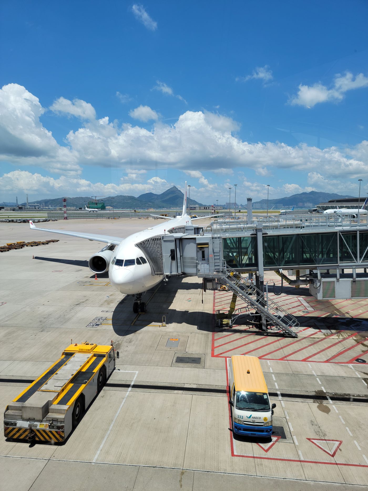A wide-body airliner parked at a boarding gate at Hong Kong International Airport under a clear sky
