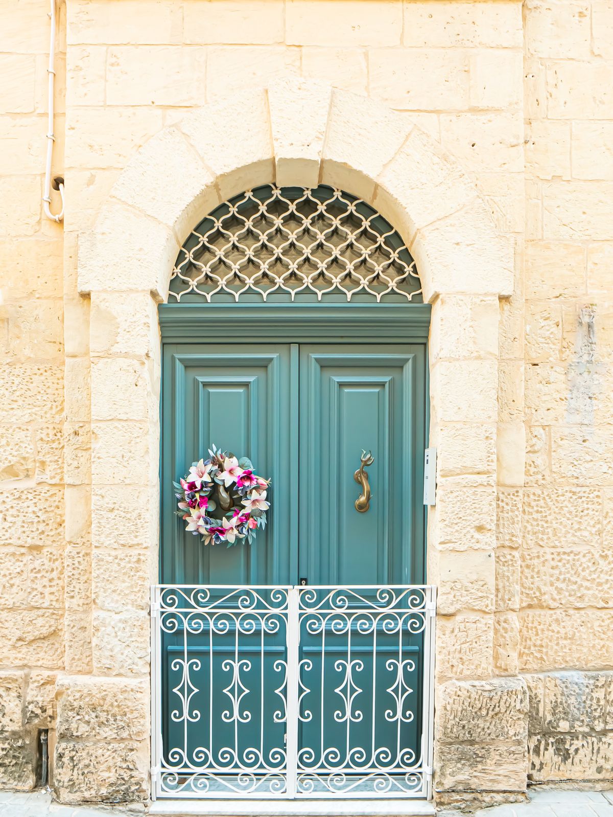A vintage teal door with a floral wreath on a stone building in Malta, exudes classic European charm. Stock Photo.