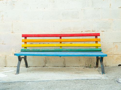 Free A colorful rainbow bench set against a rustic stone wall, perfect for lively urban outdoor spaces. Stock Photo