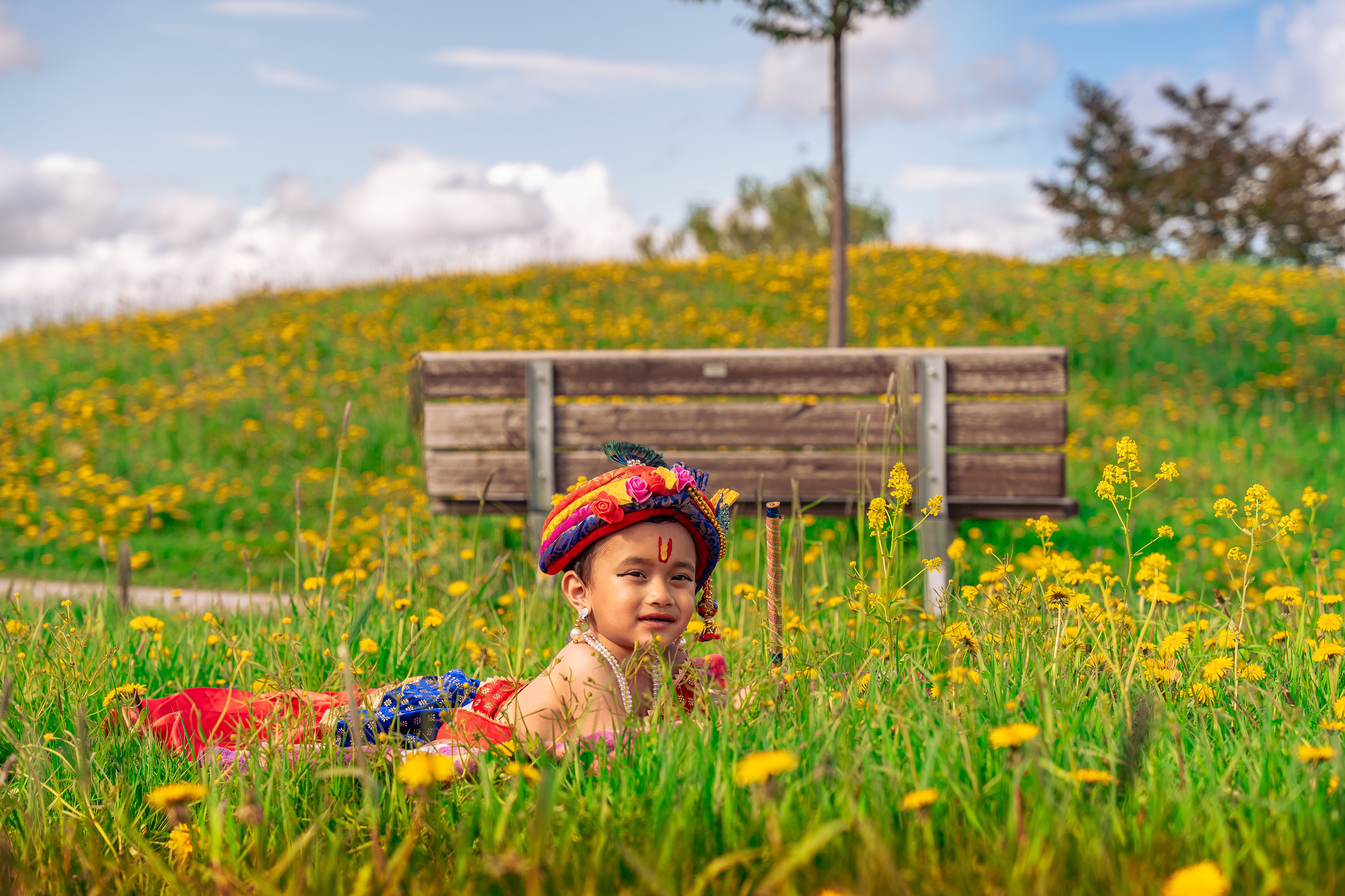 A young boy in traditional Krishna attire enjoying a summer day in a vibrant flower field.
