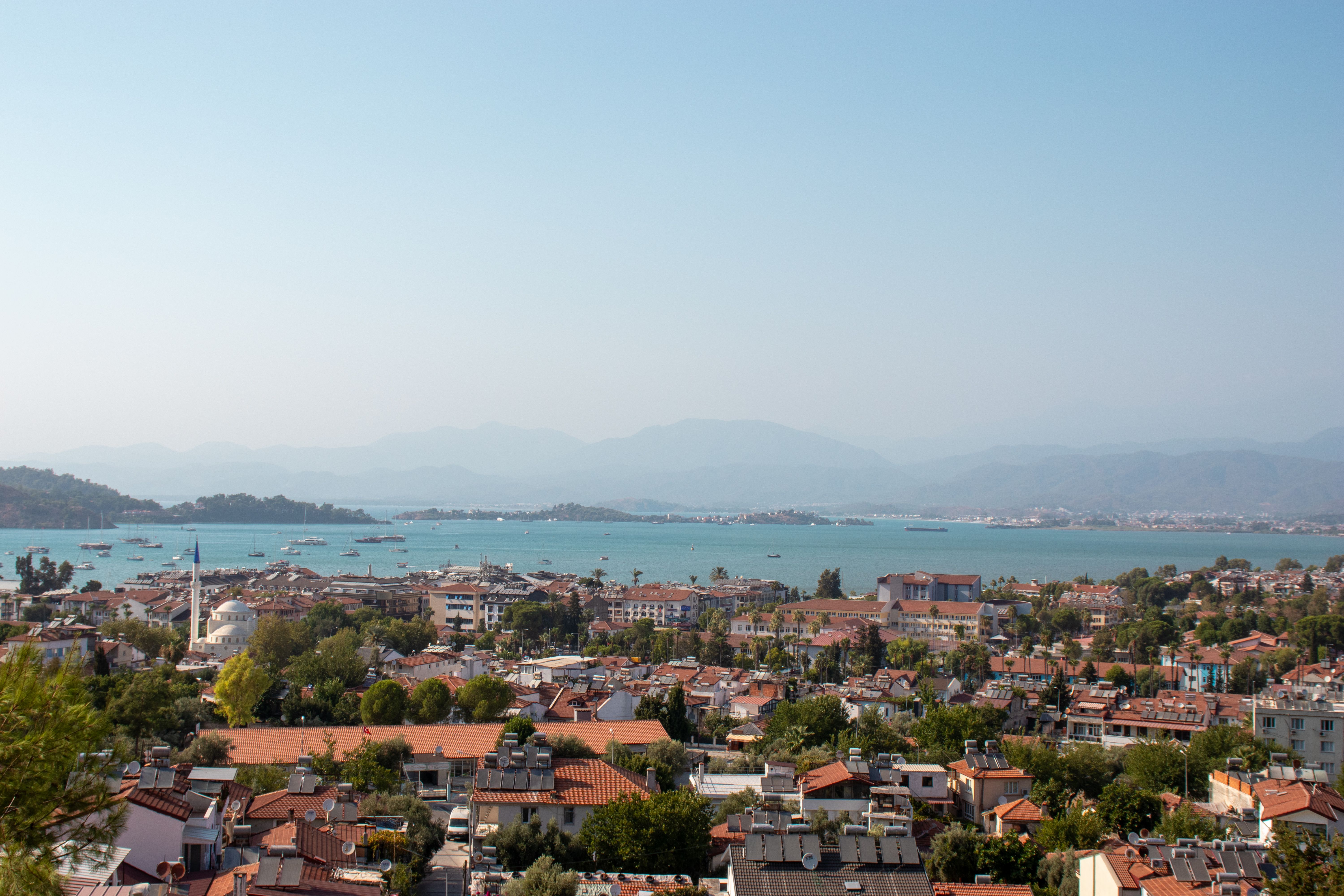 A beautiful aerial view of Fethiye, Turkey, showcasing the picturesque cityscape and the expansive Aegean Sea under a clear summer sky.