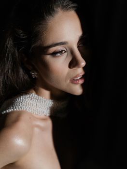 Close-up portrait of a young woman in soft lighting with pearl accessories and expressing elegance.