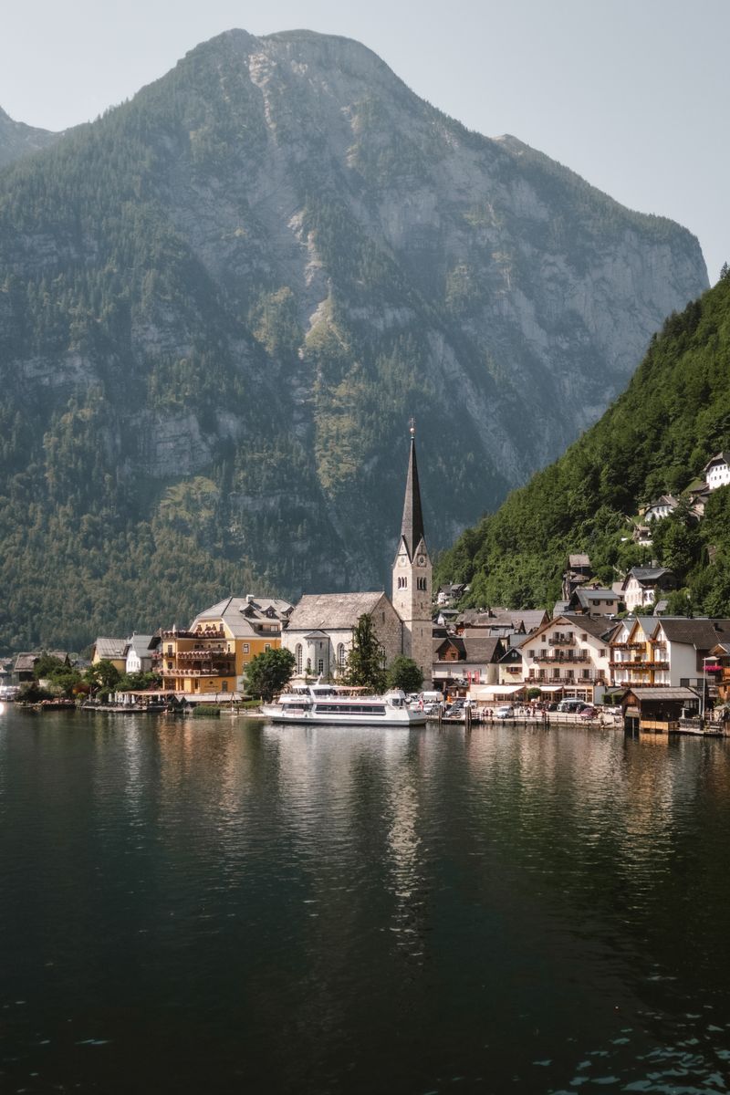 Satul Hallstatt reflectat în lacul alpin, cu munții pe fundal