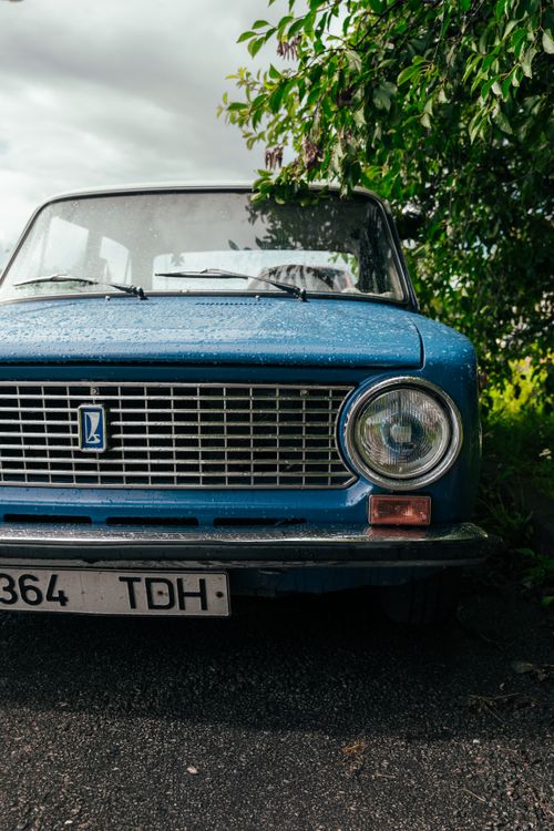 Free Close-up of a vintage blue Lada car parked outdoors under a tree with raindrops visible. Stock Photo