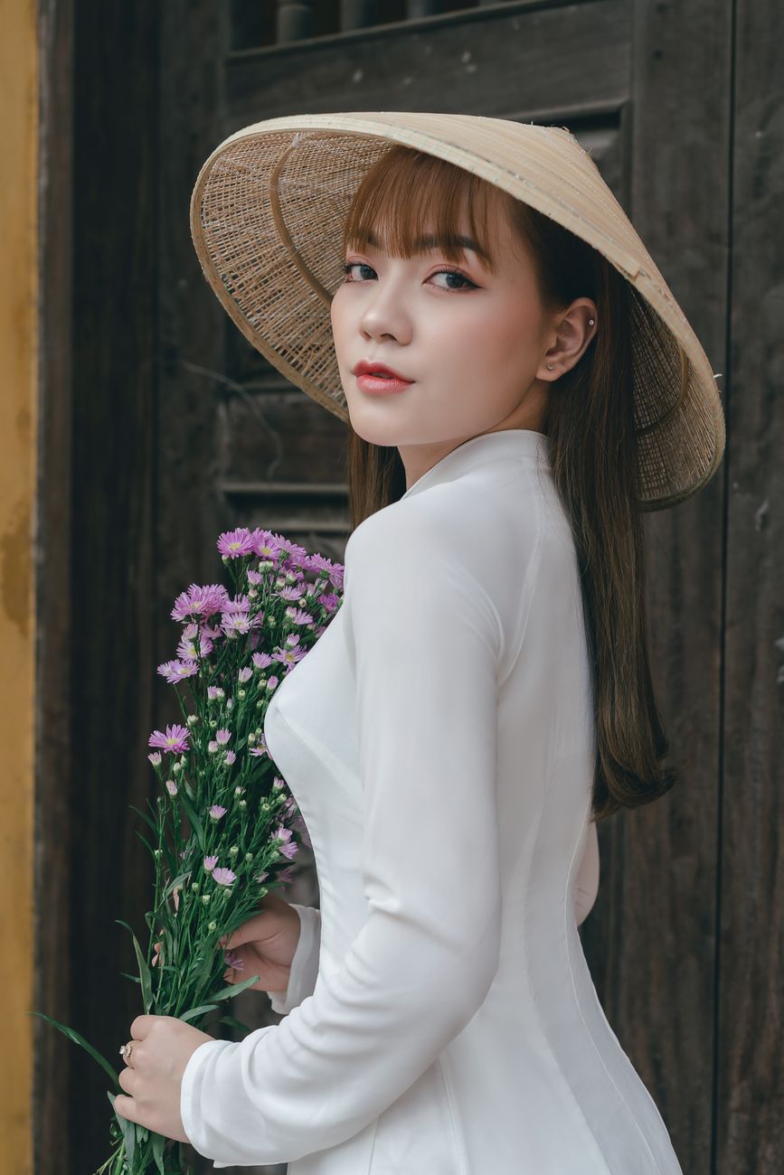Elegant woman in conical hat holding flowers, showcasing traditional fashion and culture.