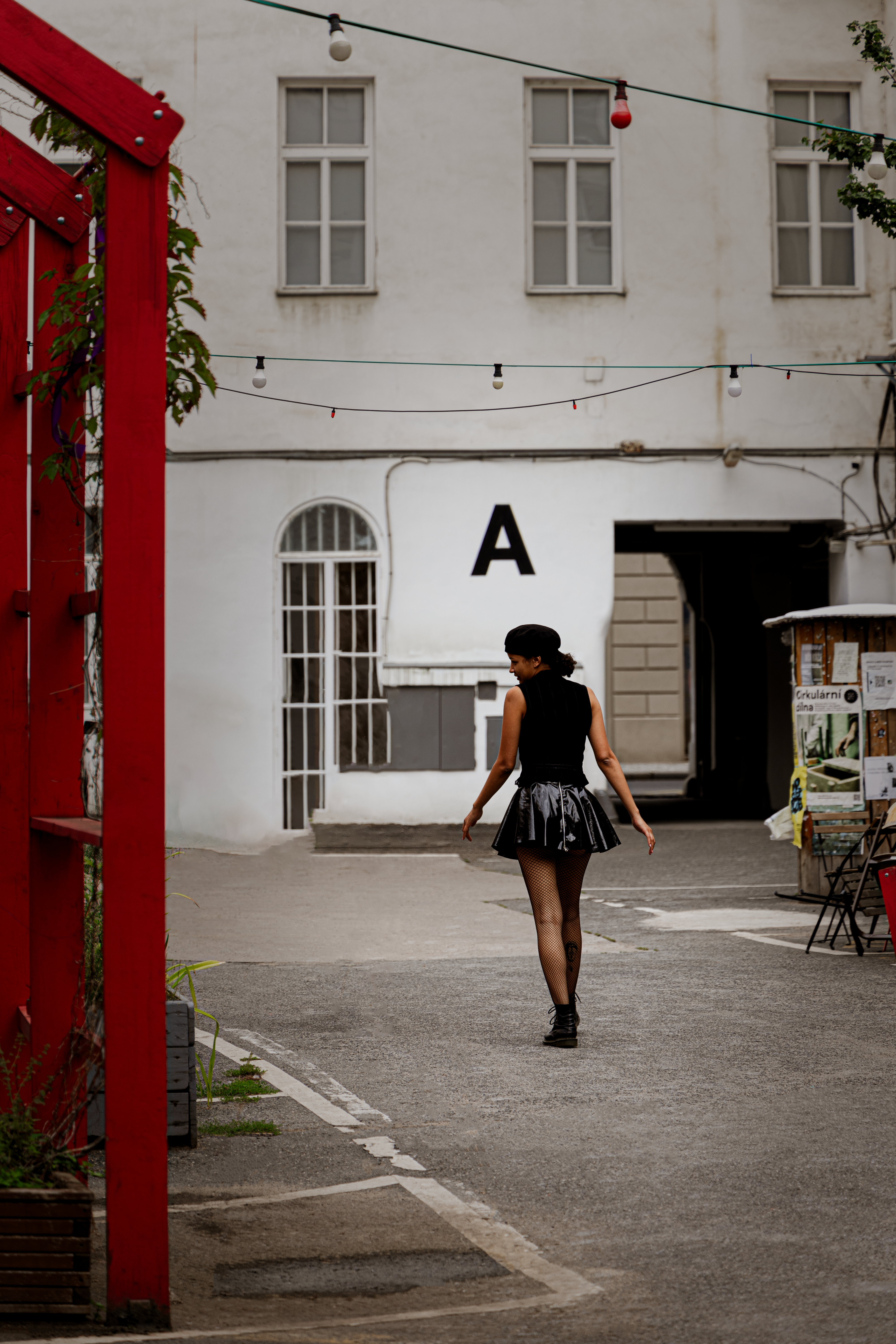 Stylish woman in a black outfit walking in a modern urban alleyway with red accents.