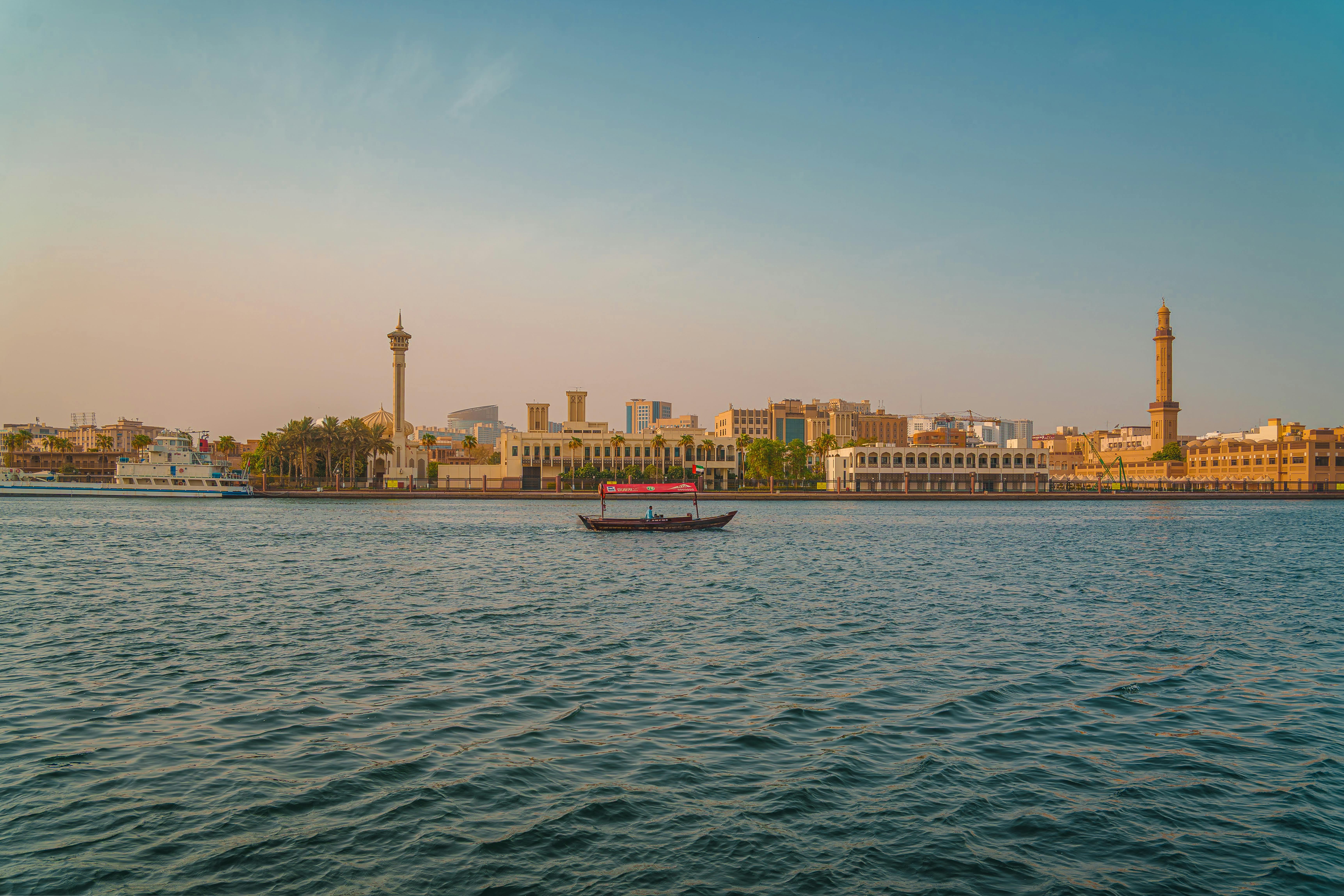 Scenic sunset view of Dubai Creek featuring traditional boats and a skyline of iconic Middle Eastern