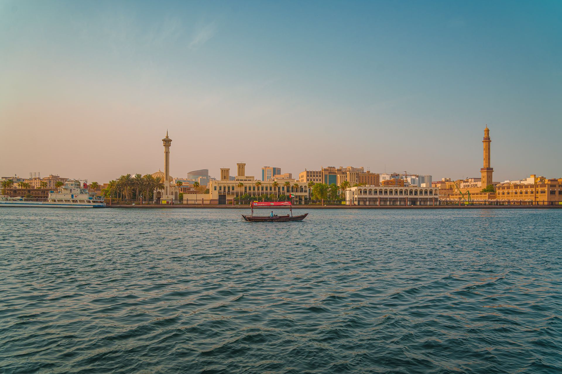 Scenic sunset view of Dubai Creek featuring traditional boats and a skyline of iconic Middle Eastern