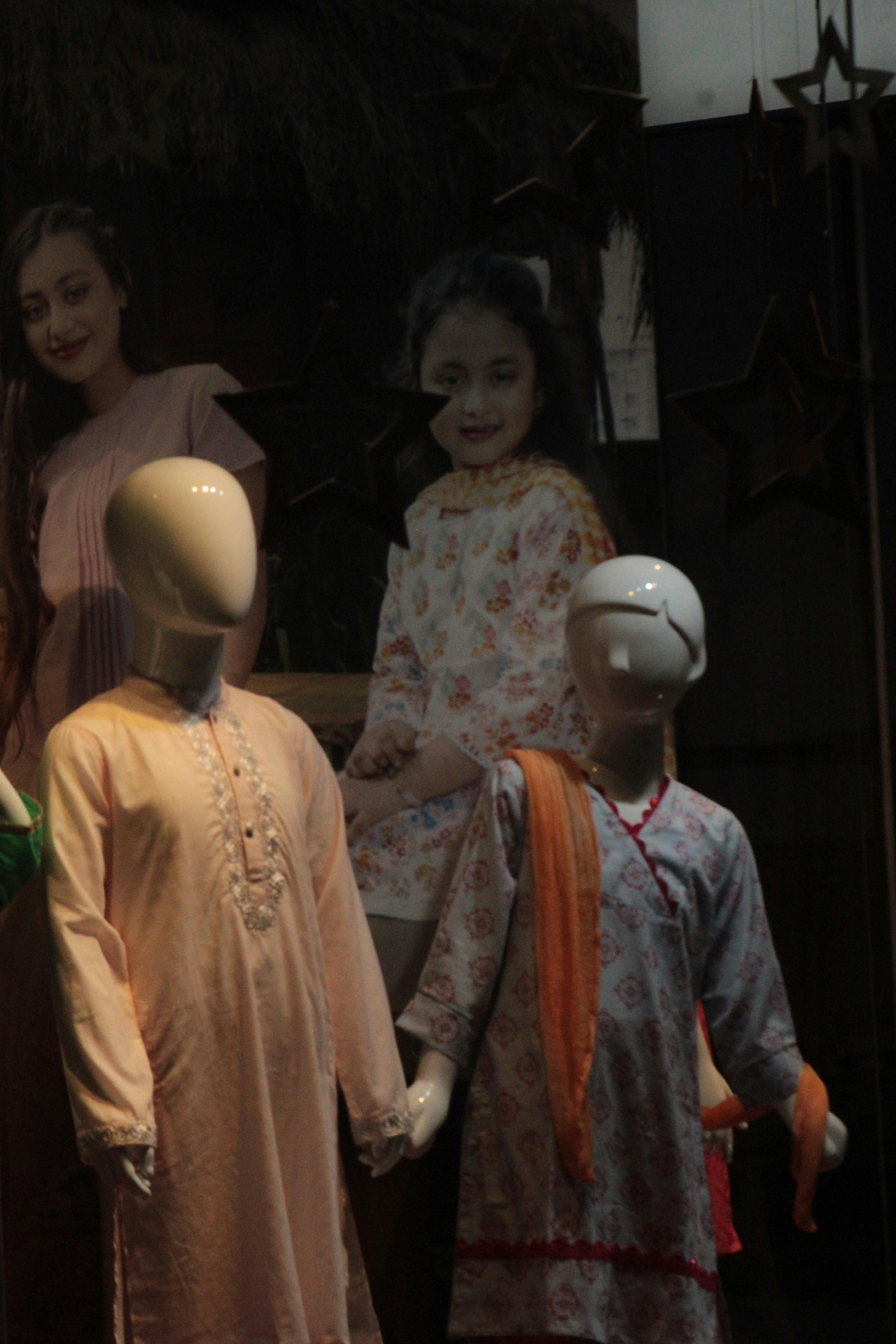 Fashion display with mannequins and children reflecting in store window.
