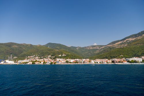 Free Charming coastal town nestled between lush mountains and vibrant blue sea under clear skies. Stock Photo