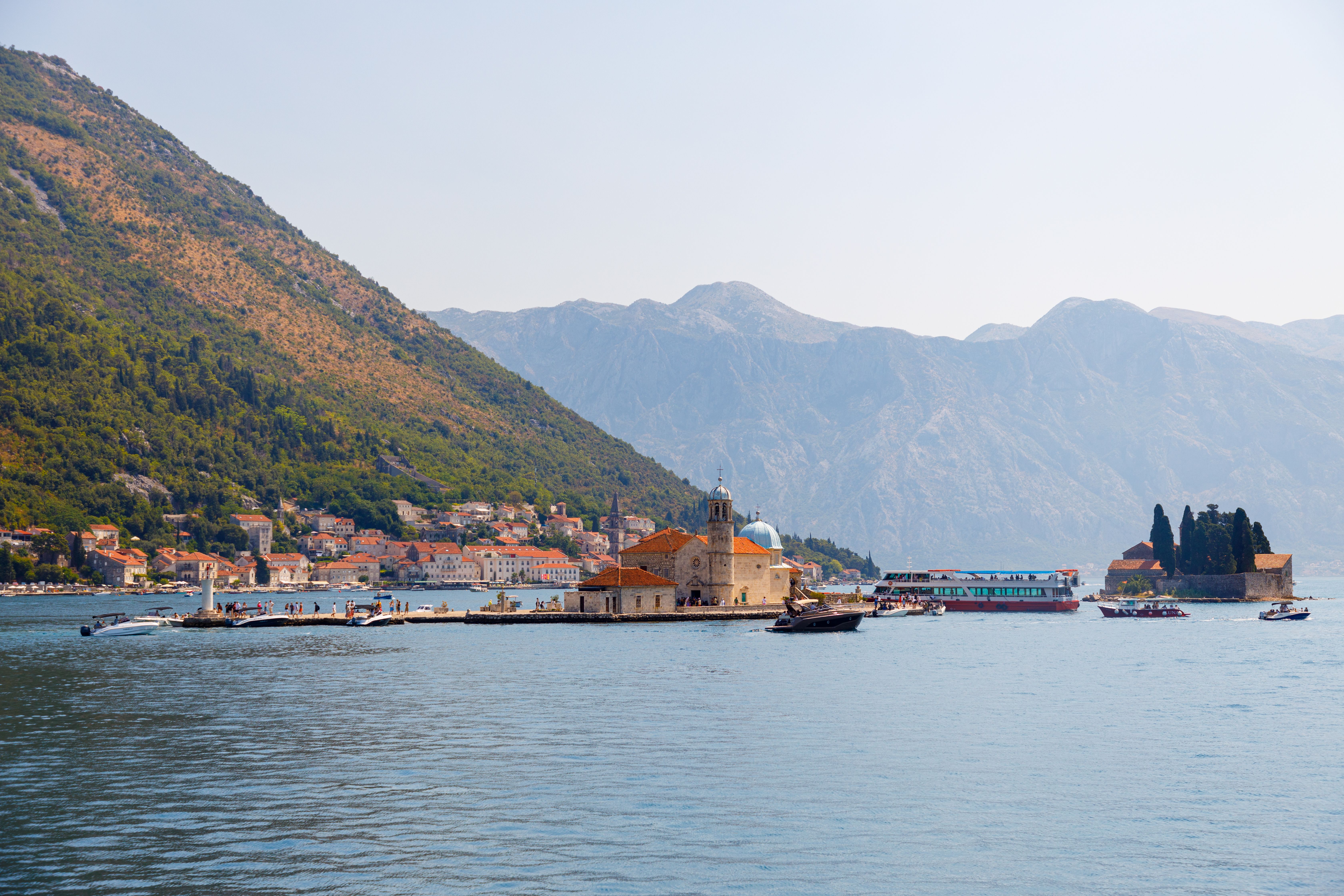 A boat cruising through the picturesque Kotor Bay in Montenegro, passing historic islands.