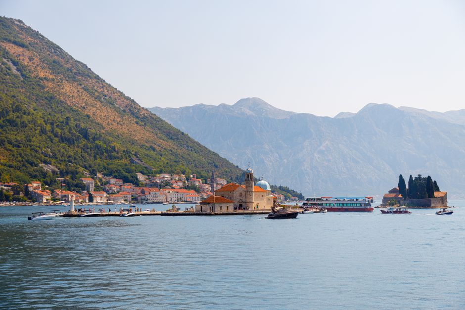 A boat cruising through the picturesque Kotor Bay in Montenegro, passing historic islands.