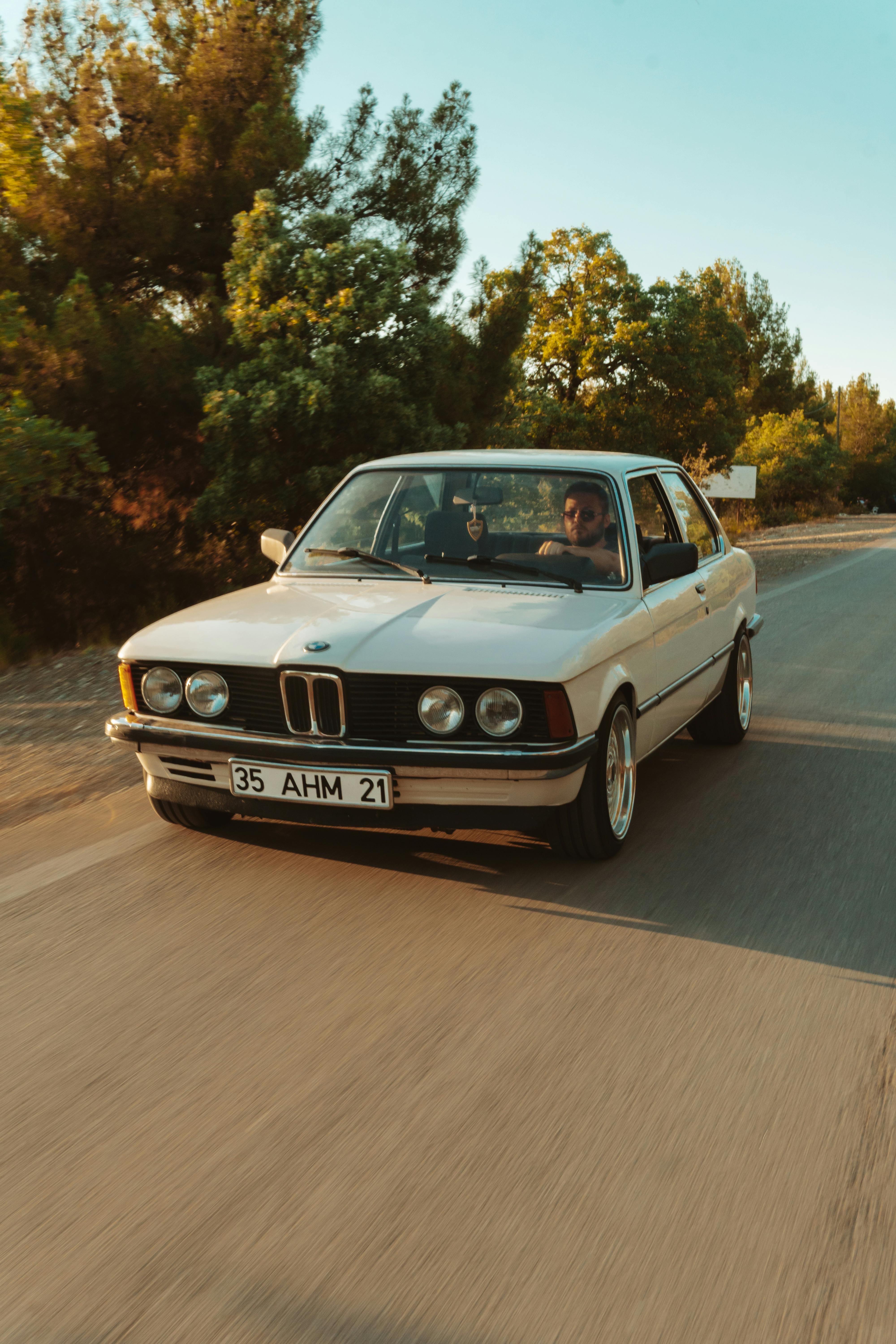 Vintage BMW driving on a picturesque road in İzmir, Türkiye, surrounded by lush greenery.