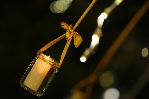 Free Close-up of a candle lit inside a glass jar with yellow ribbon, creating a warm ambient glow. Stock Photo