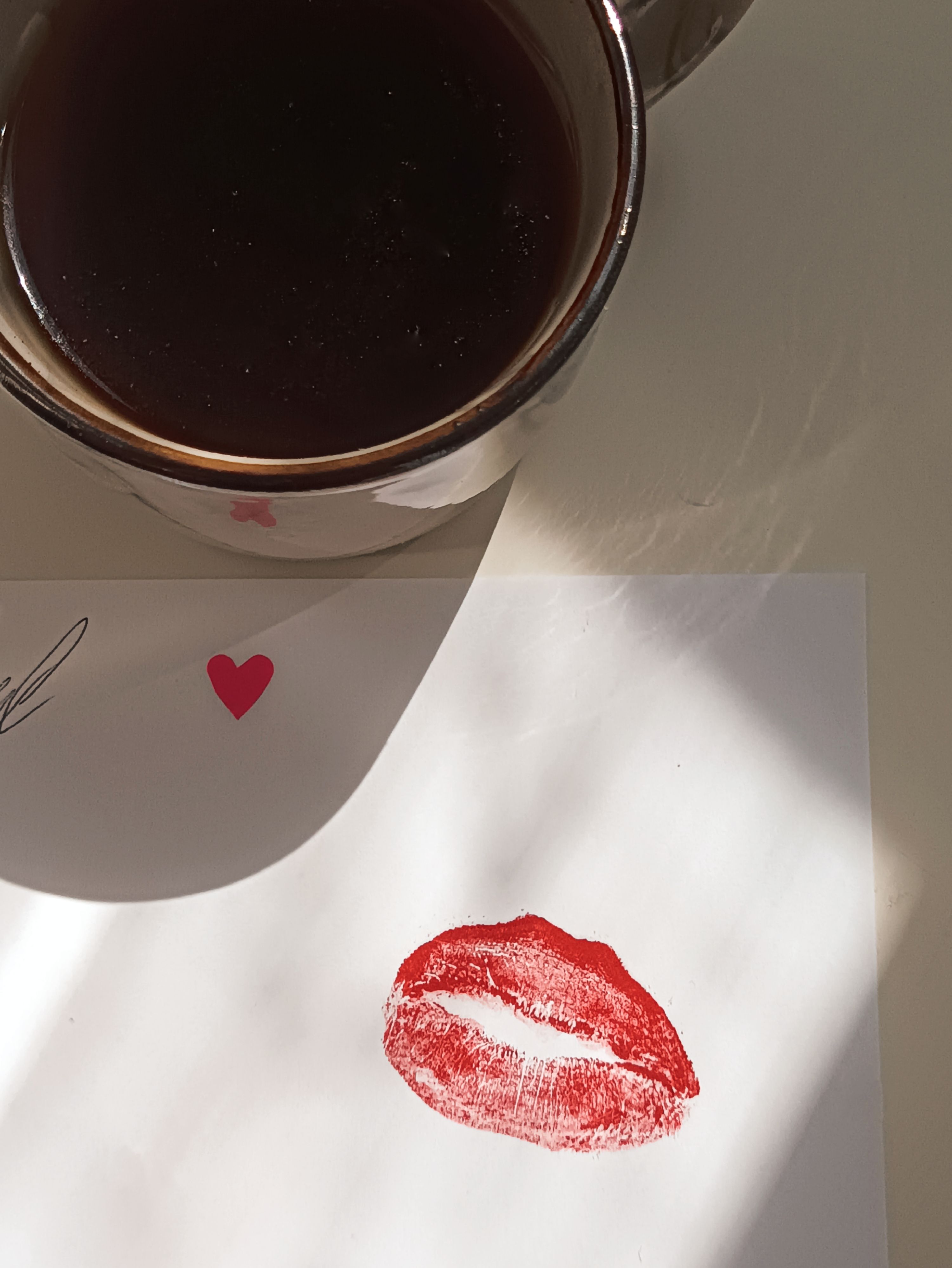 Close-up of a love note with lipstick kiss and a cup of coffee.