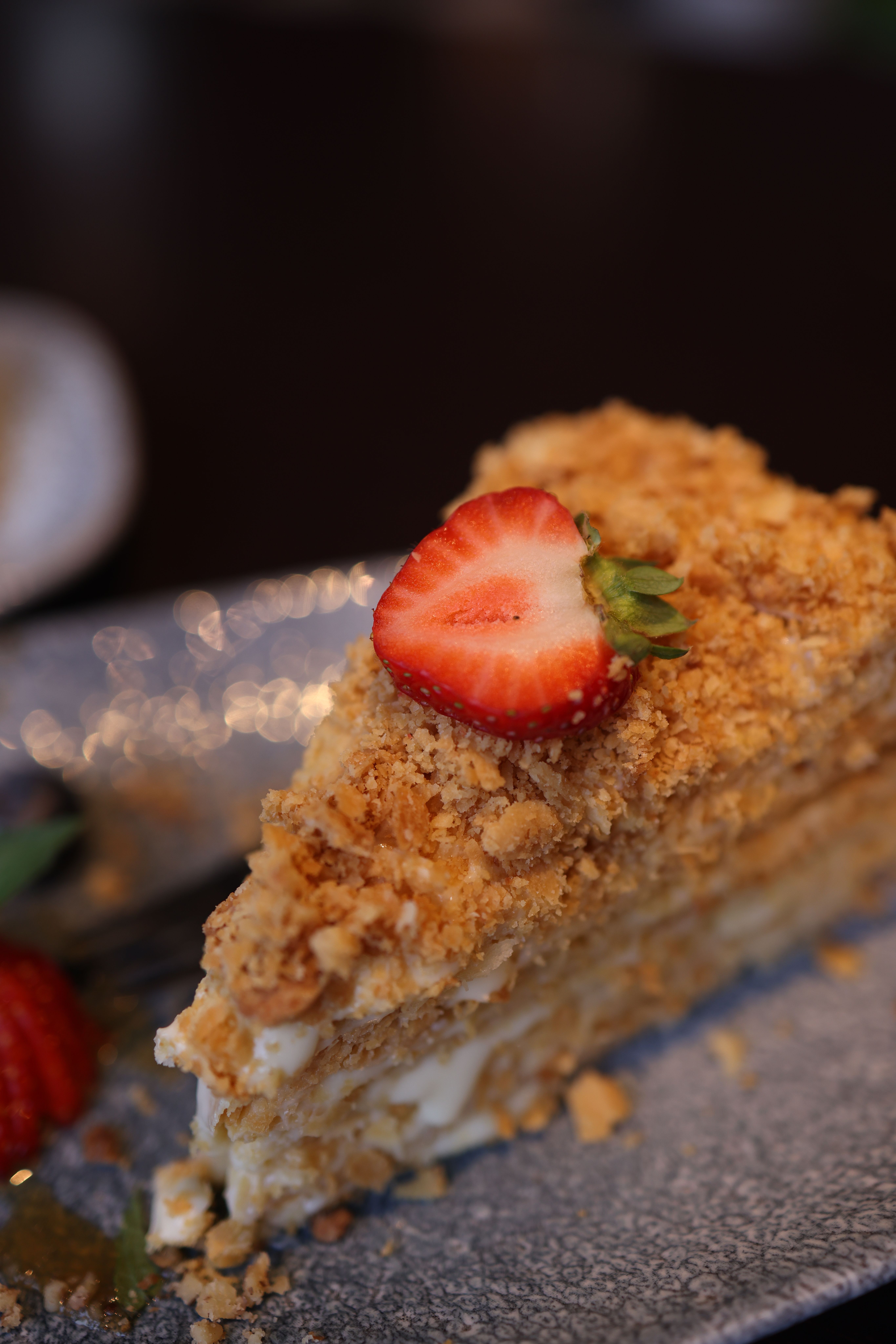 A frosted strawberry crunch cake sliced to show pink cake layers and cream cheese frosting, with the outside coated in golden cookie and strawberry crumb topping.