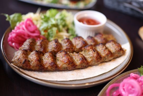Ridged grilled kofta kebab on flatbread with pink pickled onions, green salad and red dipping sauce