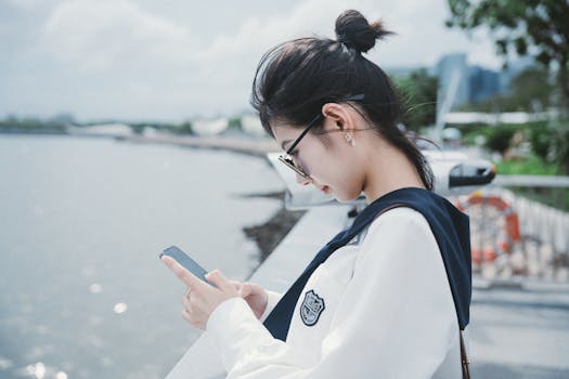 Profile of young woman using a smartphone by a waterfront on a sunny day.