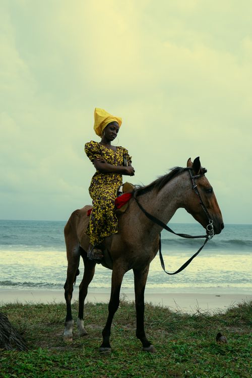 Free A woman in traditional African attire poses on horseback along the beach, showcasing cultural elegance. Stock Photo