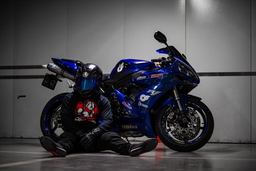 Free A motorcycle rider in black gear sits by a blue sports bike indoors, showing urban style. Stock Photo