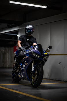 A motorcyclist on a blue sport bike in a dimly lit parking garage.