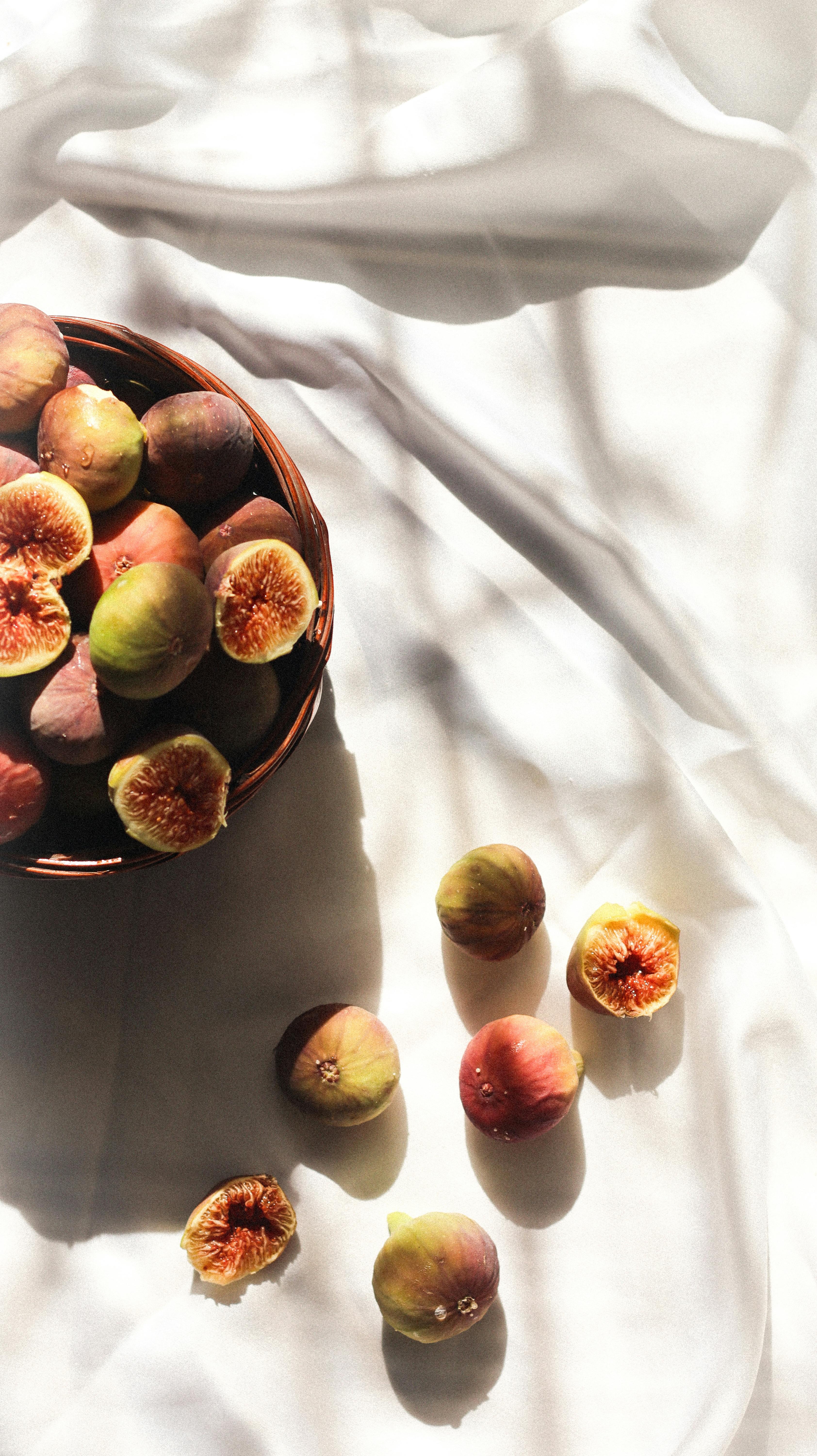 Beautiful artistic arrangement of fresh figs in a bowl with soft natural lighting and shadows on fabric.