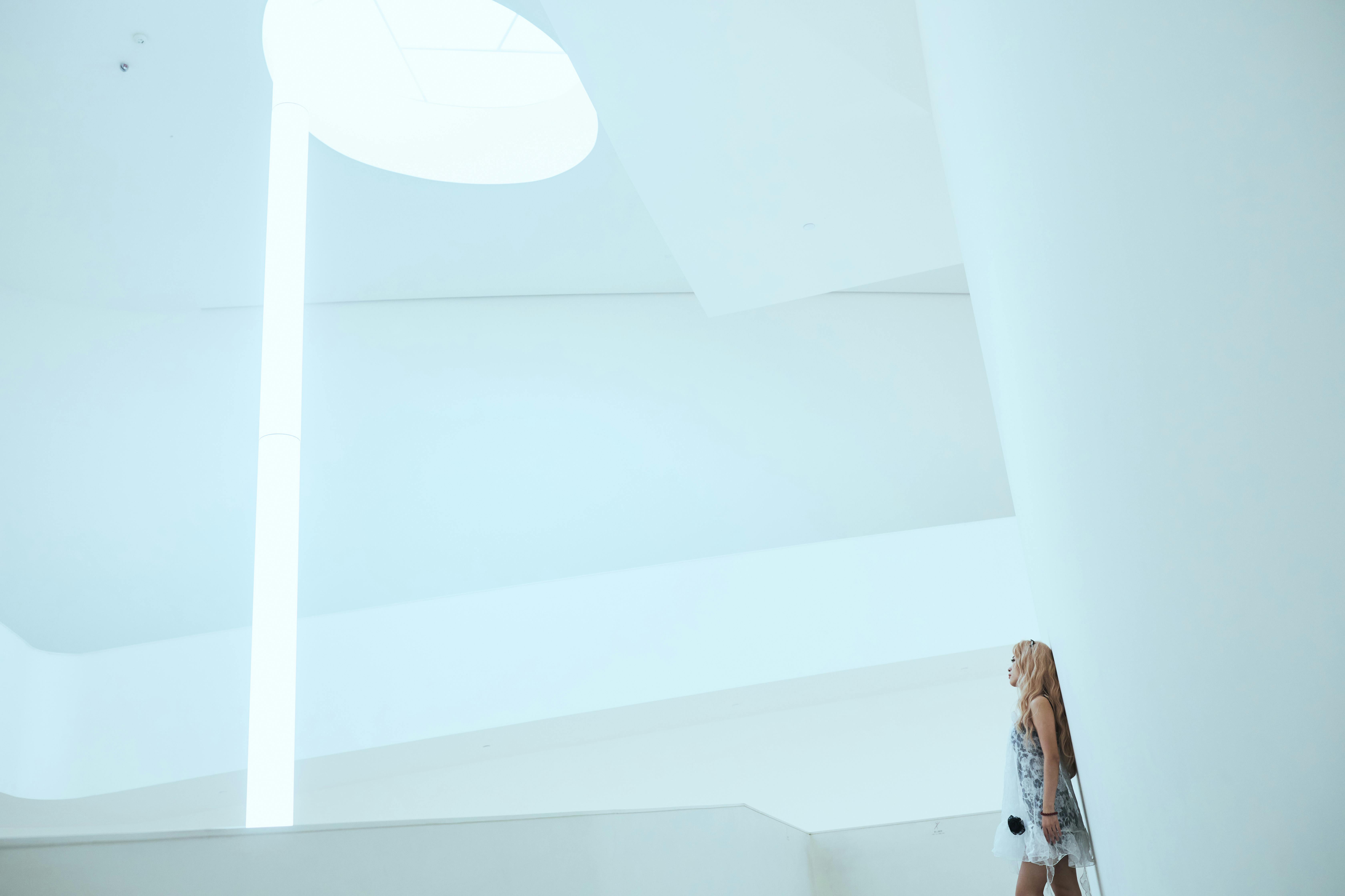 Free A woman stands in a bright, minimalist interior architecture, under natural skylight. Stock Photo