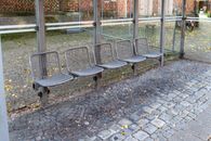 An empty bus shelter with metal mesh chairs on a cobblestone street.