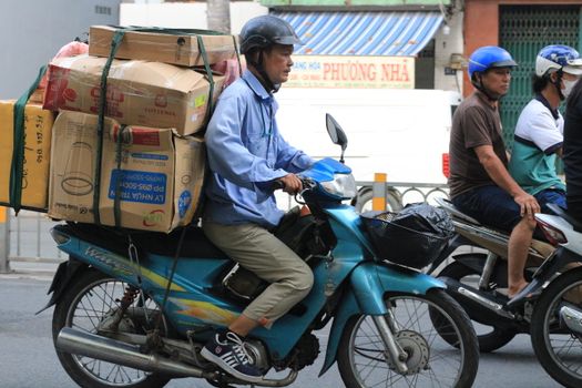 A man rides a motorbike carrying multiple boxes on a busy street in Ho Chi Minh City, Vietnam.