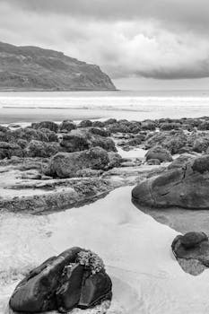 A dramatic black and white view of a rocky beach with cliffs in Scotland.