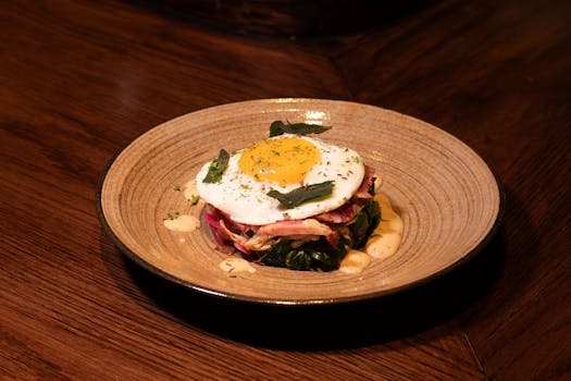A savory breakfast plate with a sunny-side-up egg, bacon, and greens on a rustic ceramic dish.