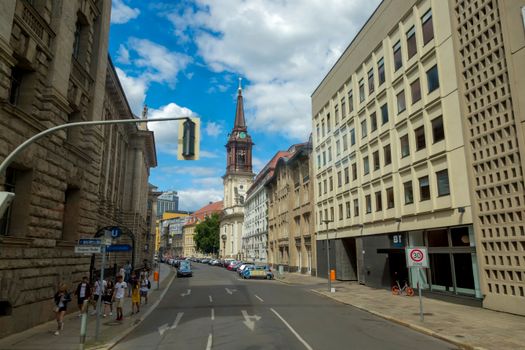 Urban scene of a Berlin street featuring historic St. Mary's Church with blue sky and pedestrians.