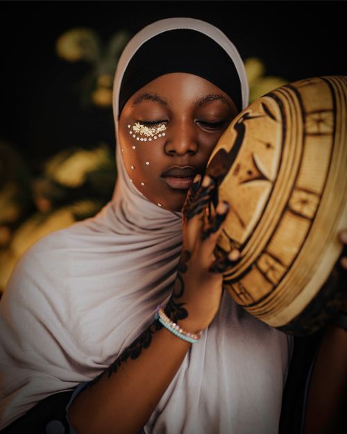 Free Young woman with facial art and hijab holding a traditional African drum. Stock Photo