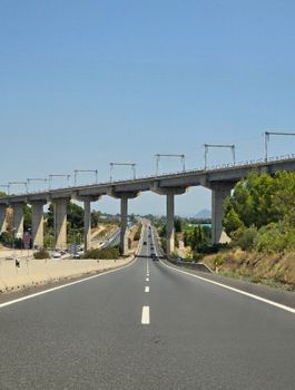 View of a highway passing under an elevated railway bridge on a clear day.