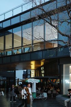People enjoy a vibrant evening at a modern urban shopping complex with glass facade and outdoor seating.