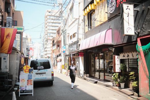 A vibrant urban street in Japan bustling with shops and a pedestrian walking under a bright sky.