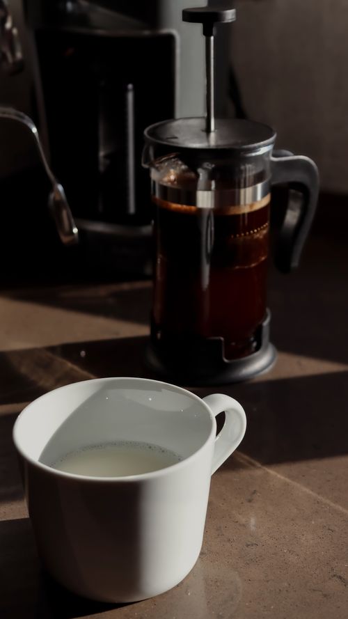 Free Warm morning light highlights a French press and coffee cup on a table. Stock Photo