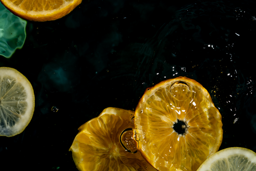 Colorful citrus slices including lemon and orange floating in dark water, highlighting freshness.