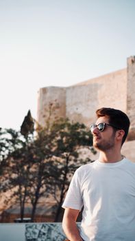 Man in sunglasses outdoors, standing against an old wall, enjoying the sunny day.