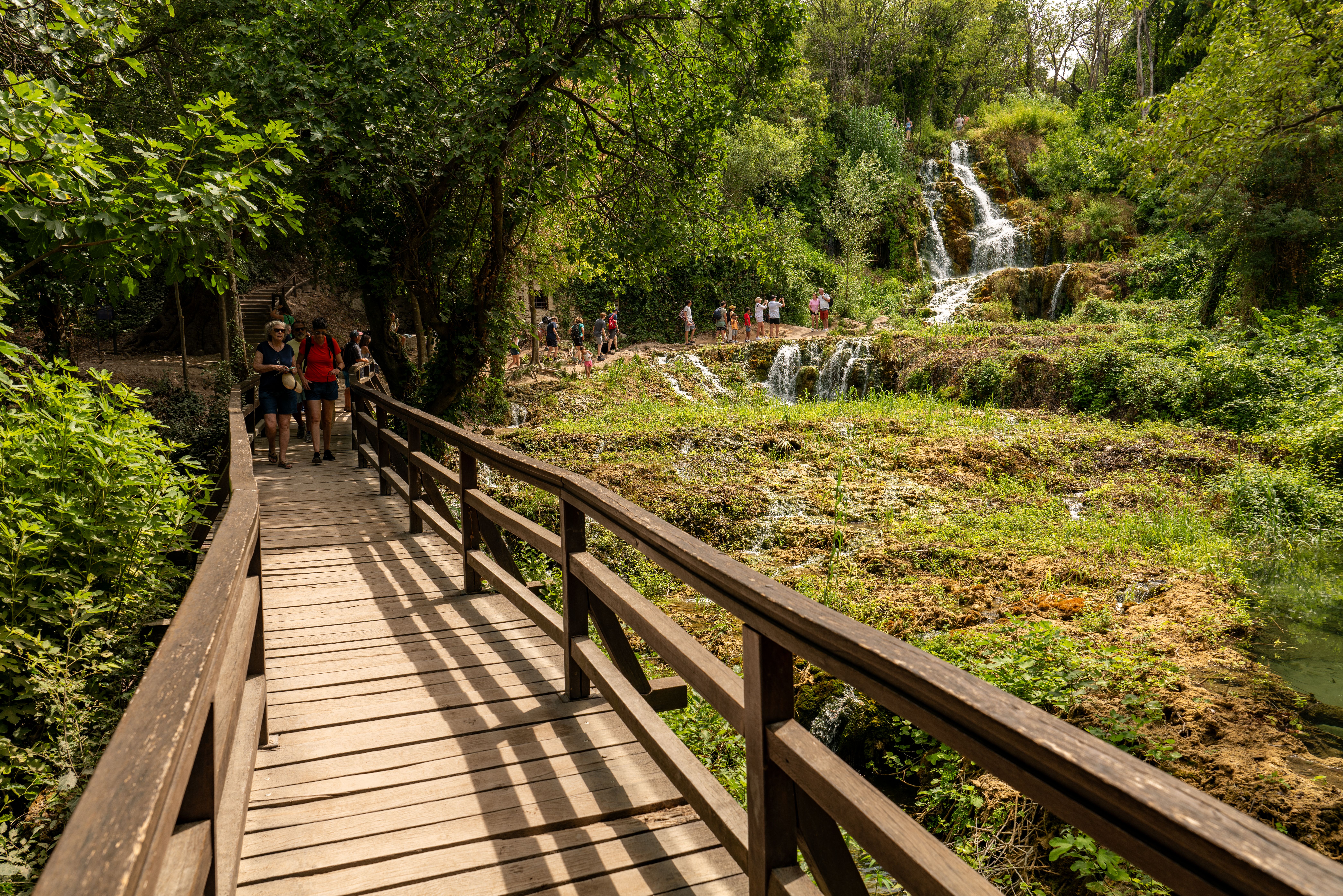 Visitors enjoy a scenic stroll along a wooden path near the Krka waterfalls in Croatia's lush summer landscape.