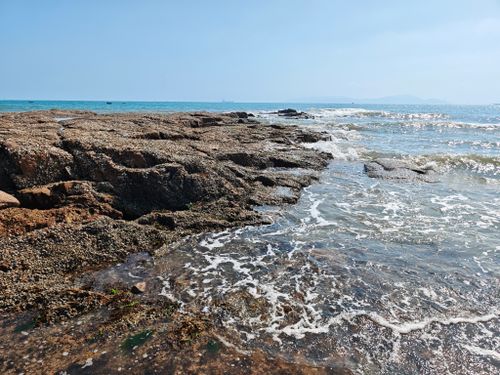 Free A sunlit rocky shoreline with gentle ocean waves under a clear sky, perfect for nature and travel themes. Stock Photo