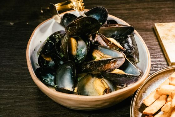 Ceramic bowl of steamed mussels in garlic herb butter broth with a small plate of fries
