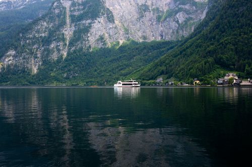 Free A serene view of a boat on a calm lake surrounded by majestic mountains and greenery. Stock Photo