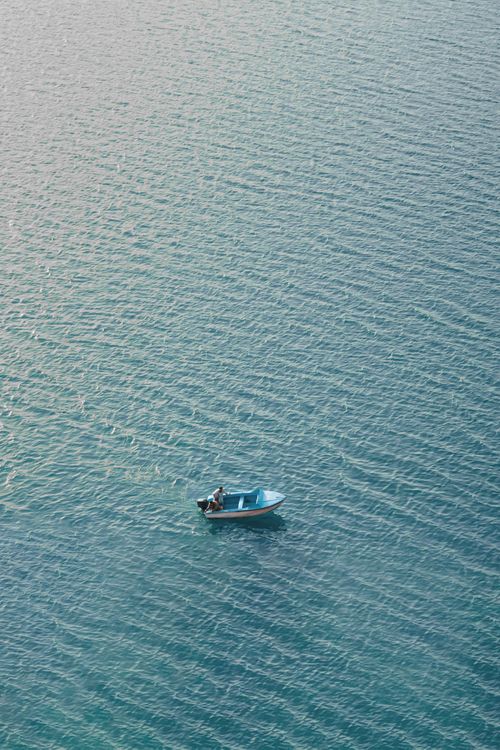 Free A lone person rowing a small boat on serene blue waters in Kabul, Afghanistan. Perfect for minimalistic themes. Stock Photo