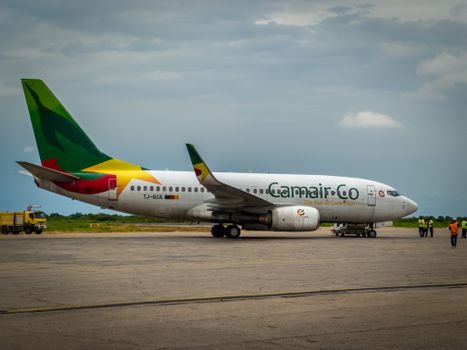 Un avion de Camair-Co stationné sur la piste de l'aéroport du Tchad avec un équipage portant des gilets de visibilité à proximité.