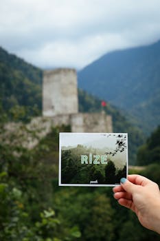 A hand holds a Rize postcard with a blurred castle backdrop.
