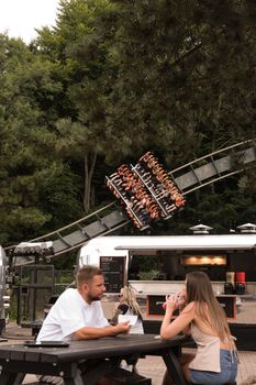 Outdoor dining near a thrilling roller coaster ride in a park setting.