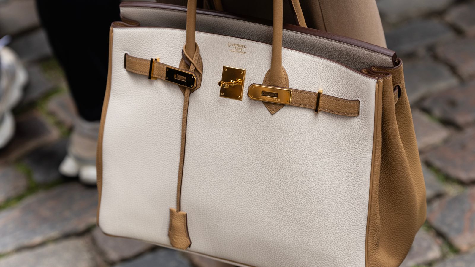 Sac à main beige élégant porté dans une rue pavée