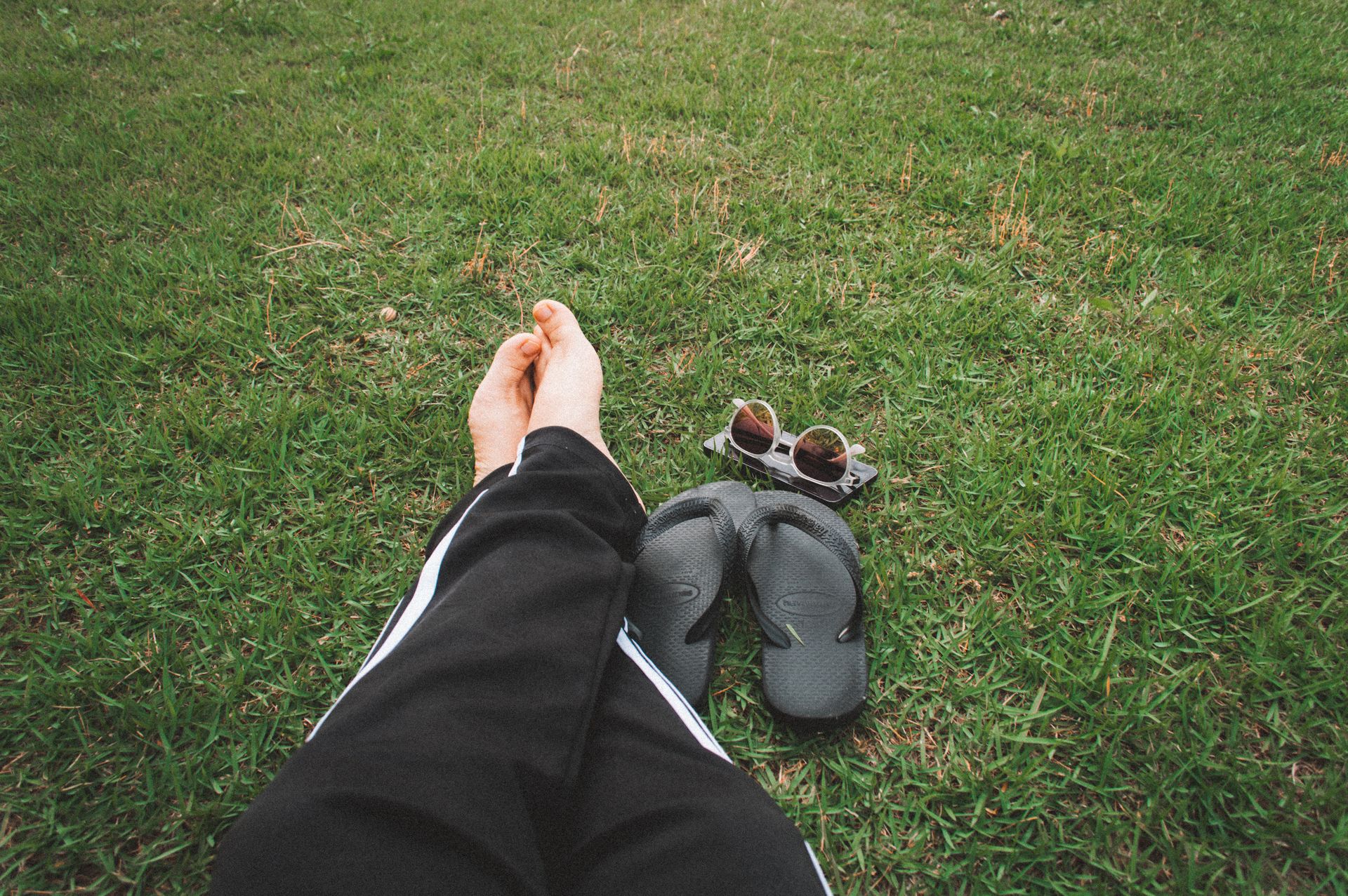 A peaceful outdoor scene shows bare feet on grass, surrounded by flip-flops and sunglasses.