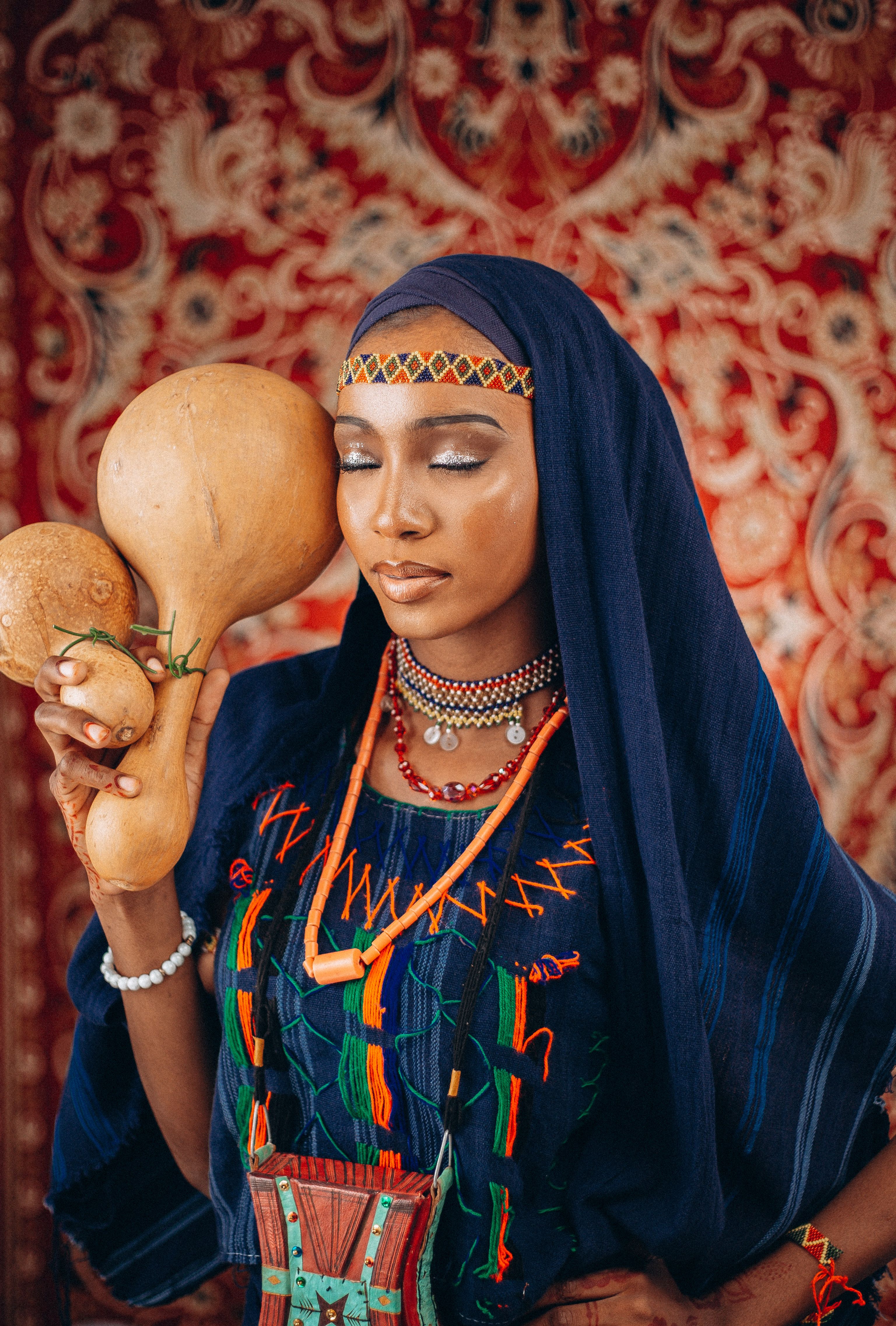 Cultural portrait of a woman with traditional dress and gourds, against a patterned backdrop.
